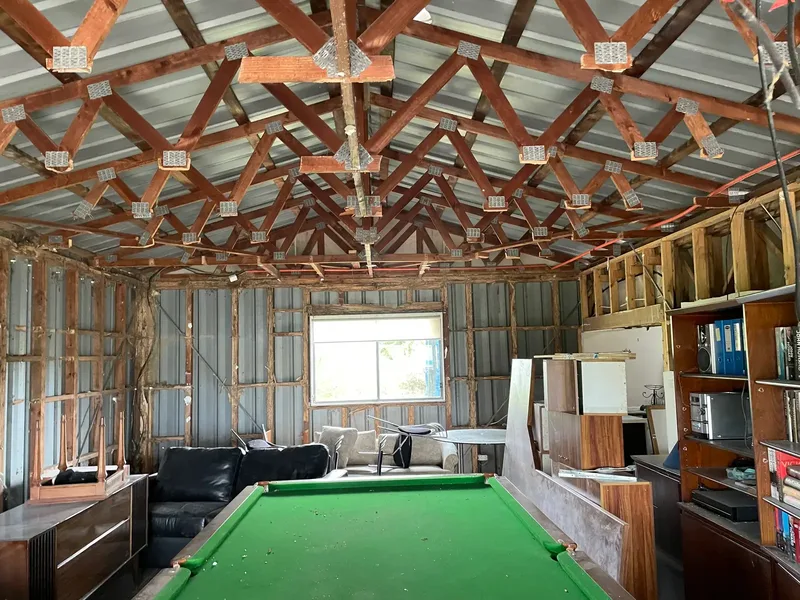 Inside a shed with the wall lining stripped off, exposing the timber wall studs and roof trusses so the framing can be checked for termite damage