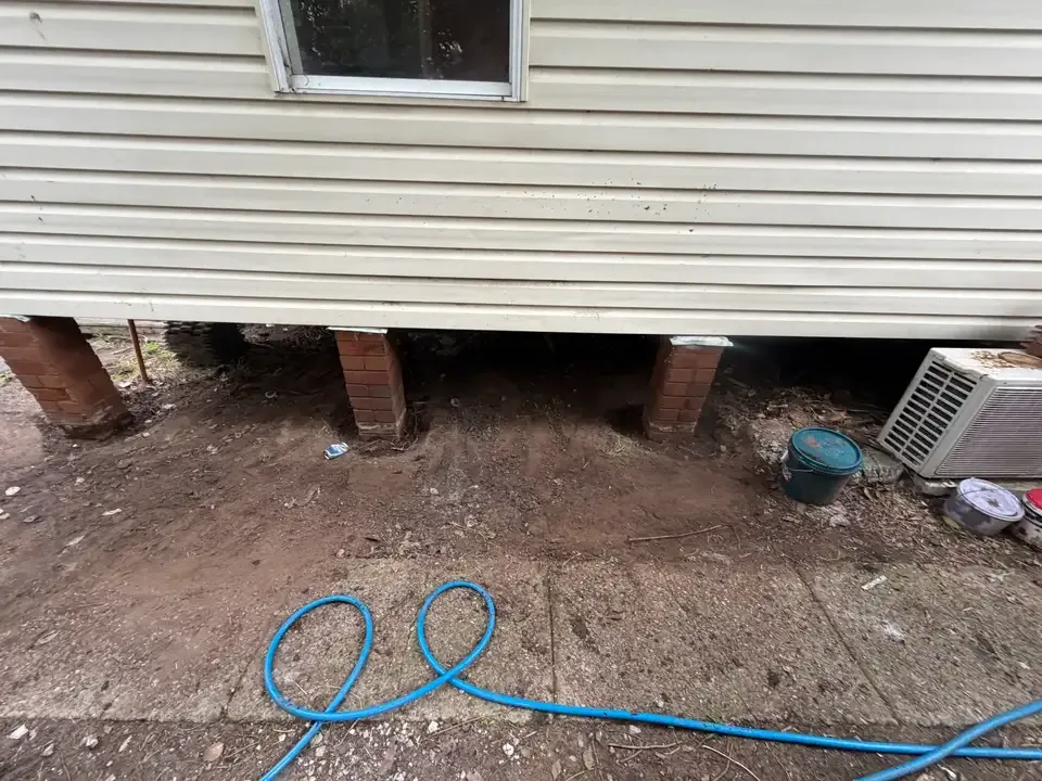 Soil dug out along the brick piers at the base of a clad house, with a hose laid out, for a chemical treated zone around the building