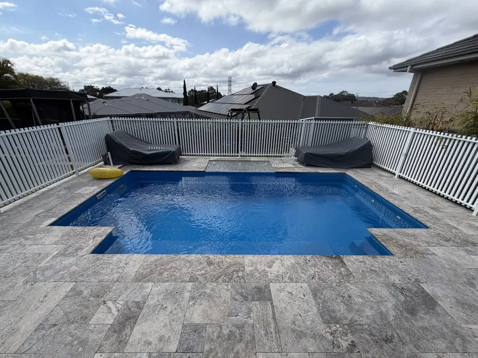Backyard swimming pool with white pool fencing and a paved deck