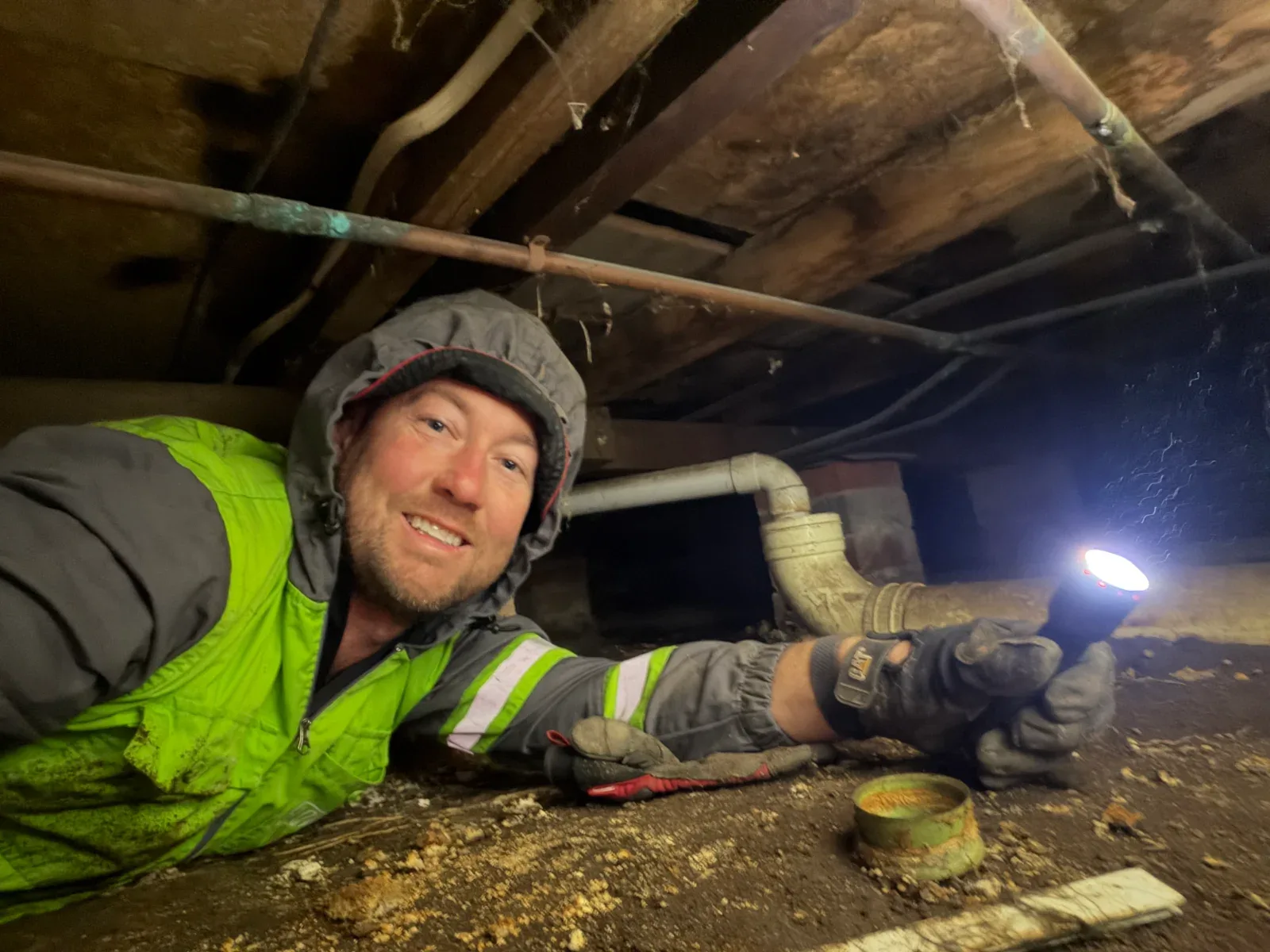 Elite inspector checking pipes and framing under a house by torchlight